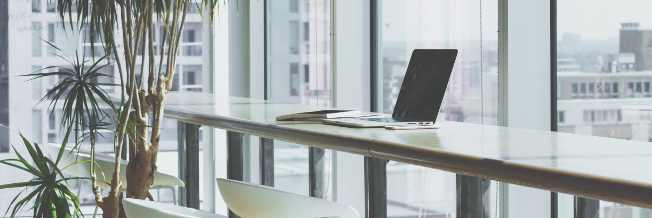 Bright office environment with a laptop on a high desk looking out of a glass fronted building