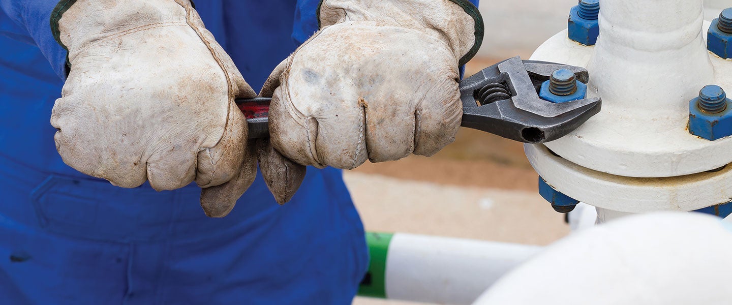 Close-up of worker's hands in protective gloves using a wrench to adjust a pipeline valve