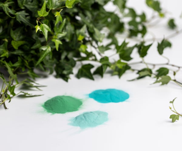 Three small piles of powder in different shades of green on a white surface below green leaves 