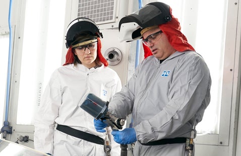 Two PPG employees in PPE inspecting spray gun