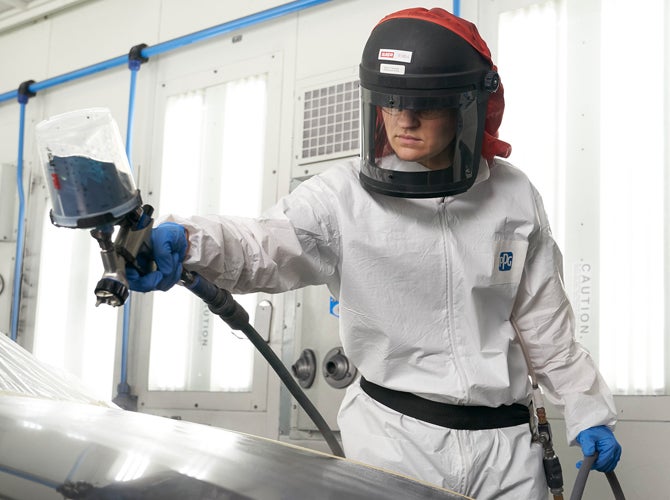 Worker in PPE using spray gun in booth