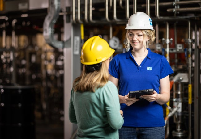 Two ladies wearing hard hats stood in a manufacturing environment