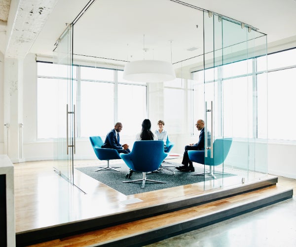 Four people sat on comfortable green chairs in a glass fronted office space