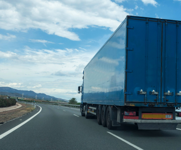 Large blue truck driving down an empty highway against a blue sky