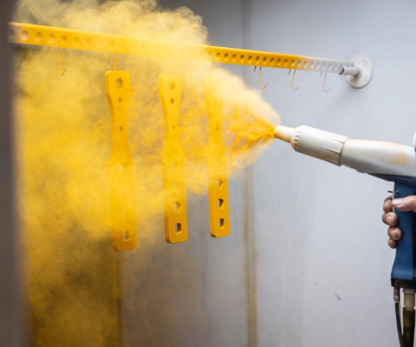 Spray gun spraying yellow powder on to hung panels