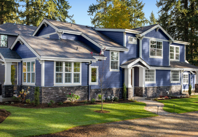 Elegant two-story family home painted in blue with white trimmings, featuring stone accents, a manicured lawn, and a winding pathway leading to the front door