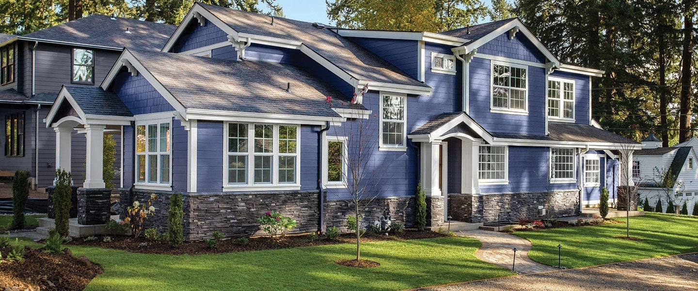 Stylish blue two-story house with stone accents and manicured garden in a suburban setting