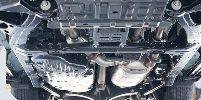 View from beneath a car showing detailed undercarriage, exhaust pipes, and protective panels