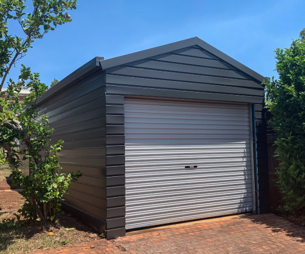 Black garage building with grey roof rolling door against a blue sky