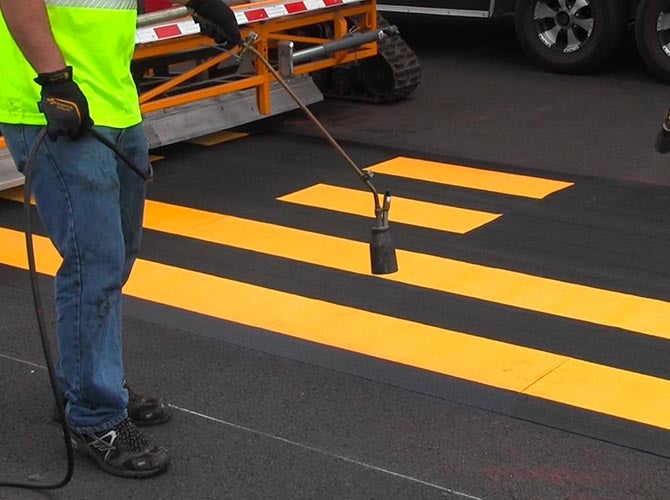 Worker using a heat torch on a roadway