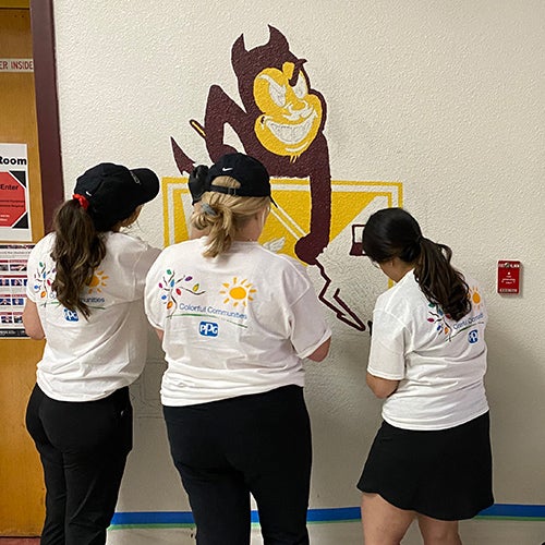 Three volunteers painting mural