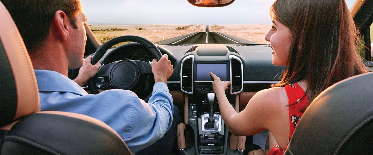 Driver and passenger traveling in a car along a straight road through a landscape