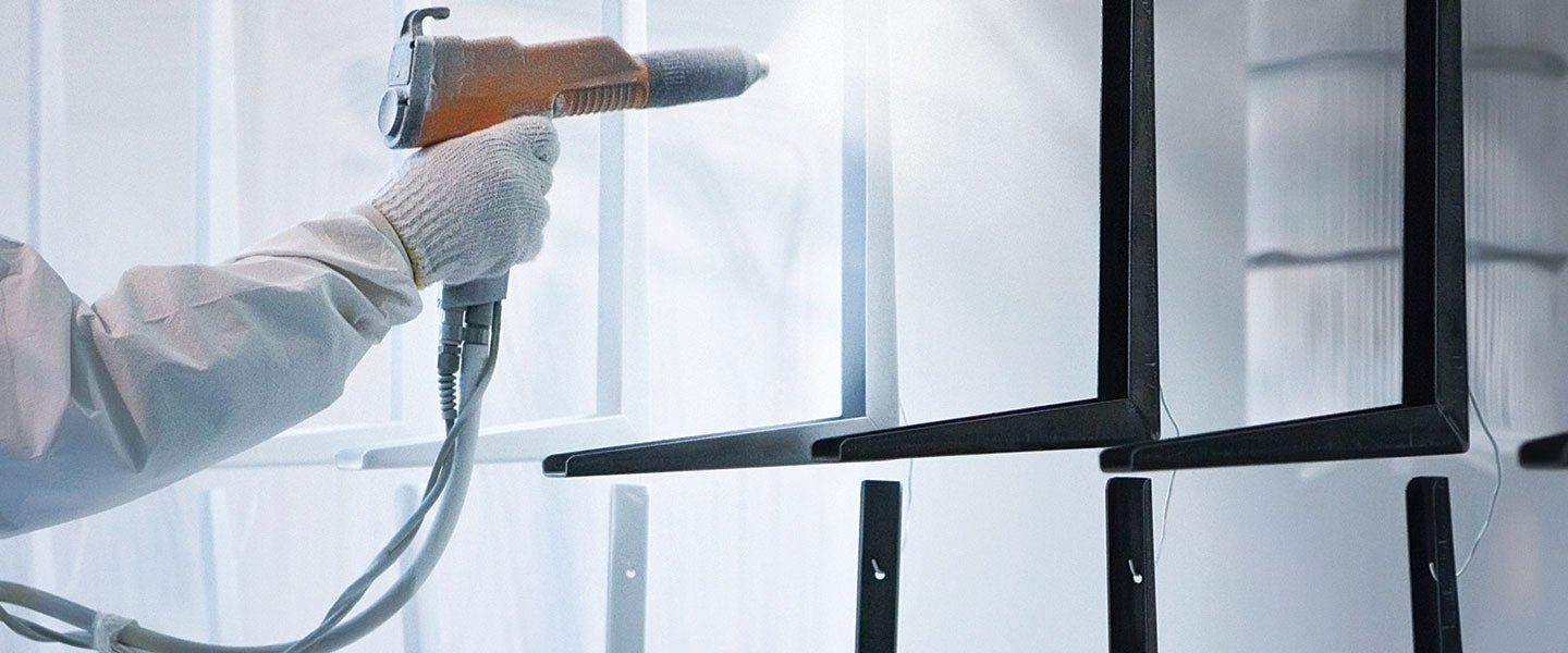 Close-up of a worker applying spray paint to metal frames in a manufacturing setting