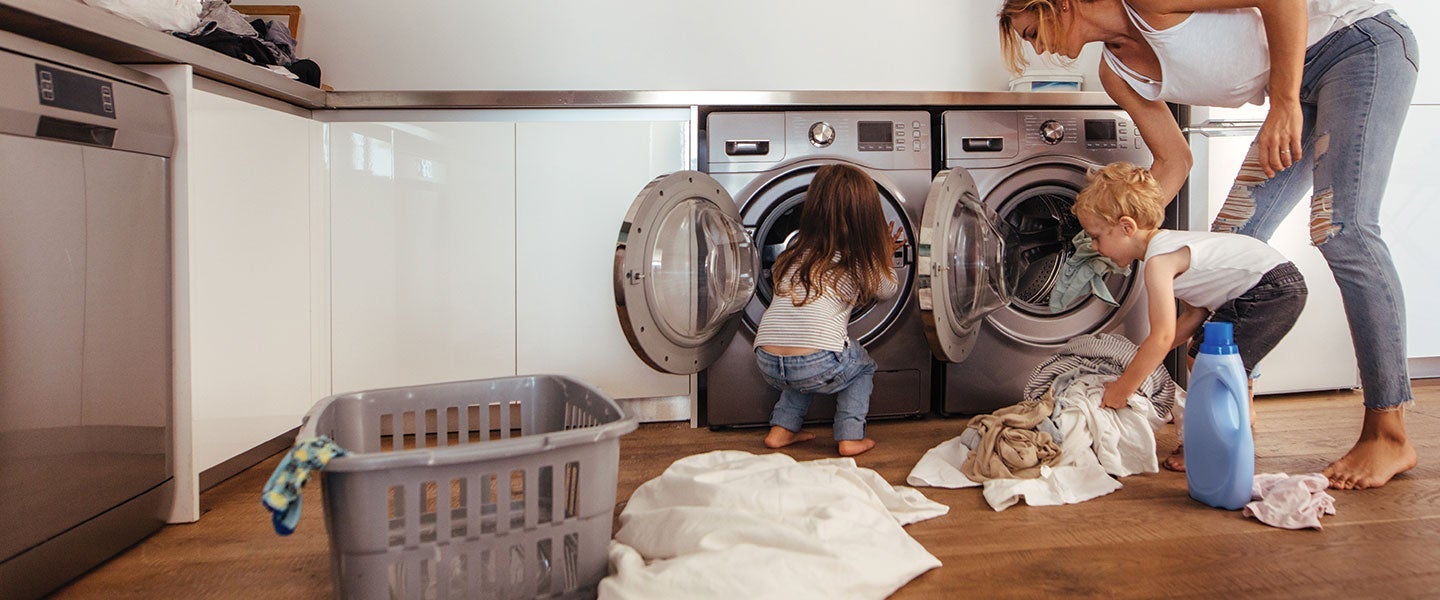 Young children helping their parent do laundry in a modern home laundry room with twin washing machines