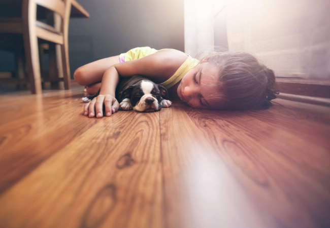 Girl and a dog lay on a wooden floor.