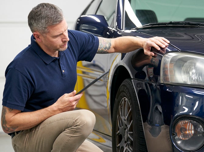 Man checking car bodywork with tablet