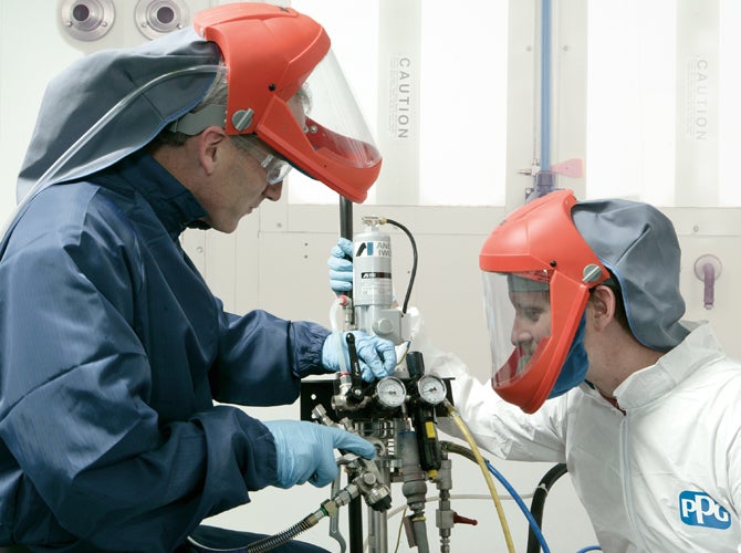 Two workers in PPE examining paint equipment