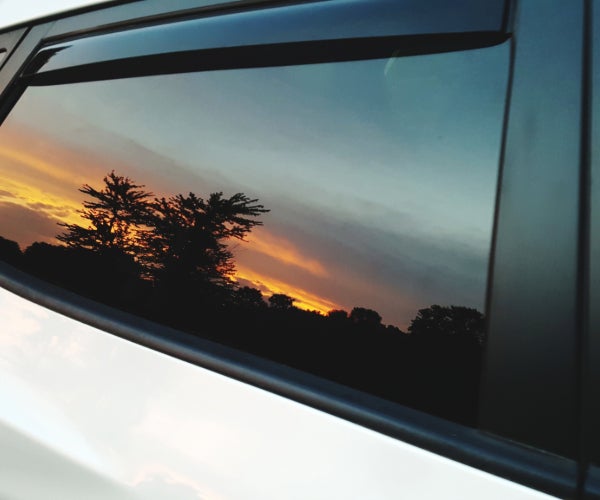 Car window reflecting a yellow and orange sunset showing the silhouette of a tree