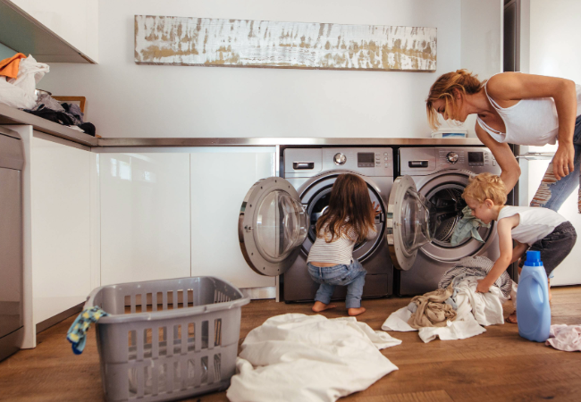 Woman and children in a kitchen loading washing into silver appliances