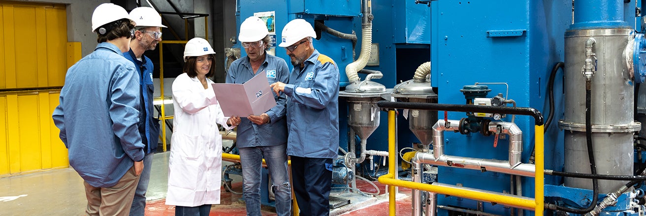 PPG workers wearing PPE in manufacturing plant whilst discussing documentation