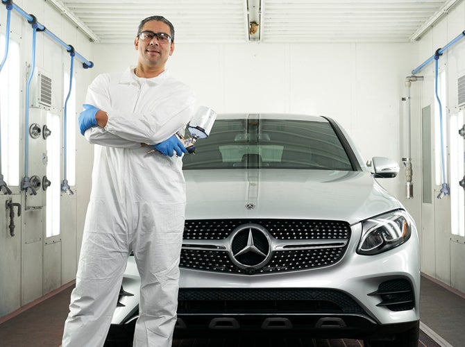 Employee with spray gun standing next to car in spray booth