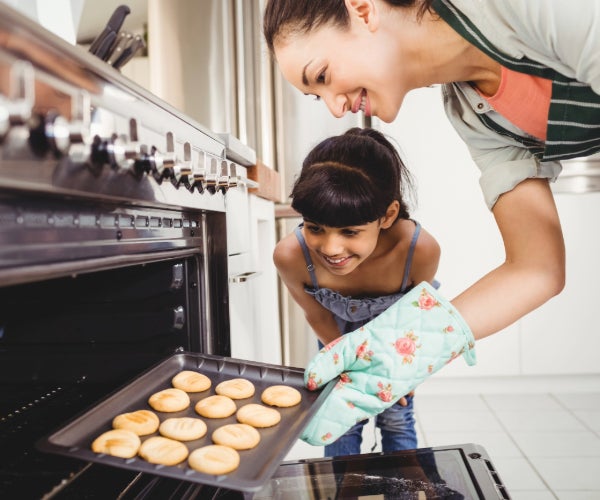 Mother and daughter taking a tray of baked cookies out of the oven