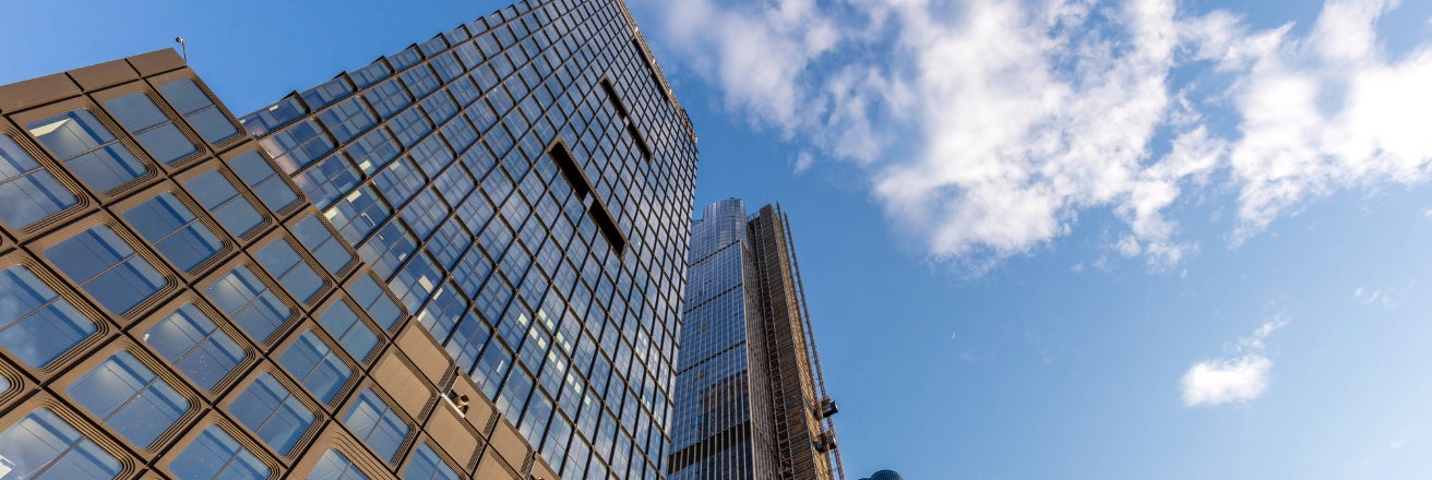 Looking up a glass fronted skyscraper towards a blue sky 