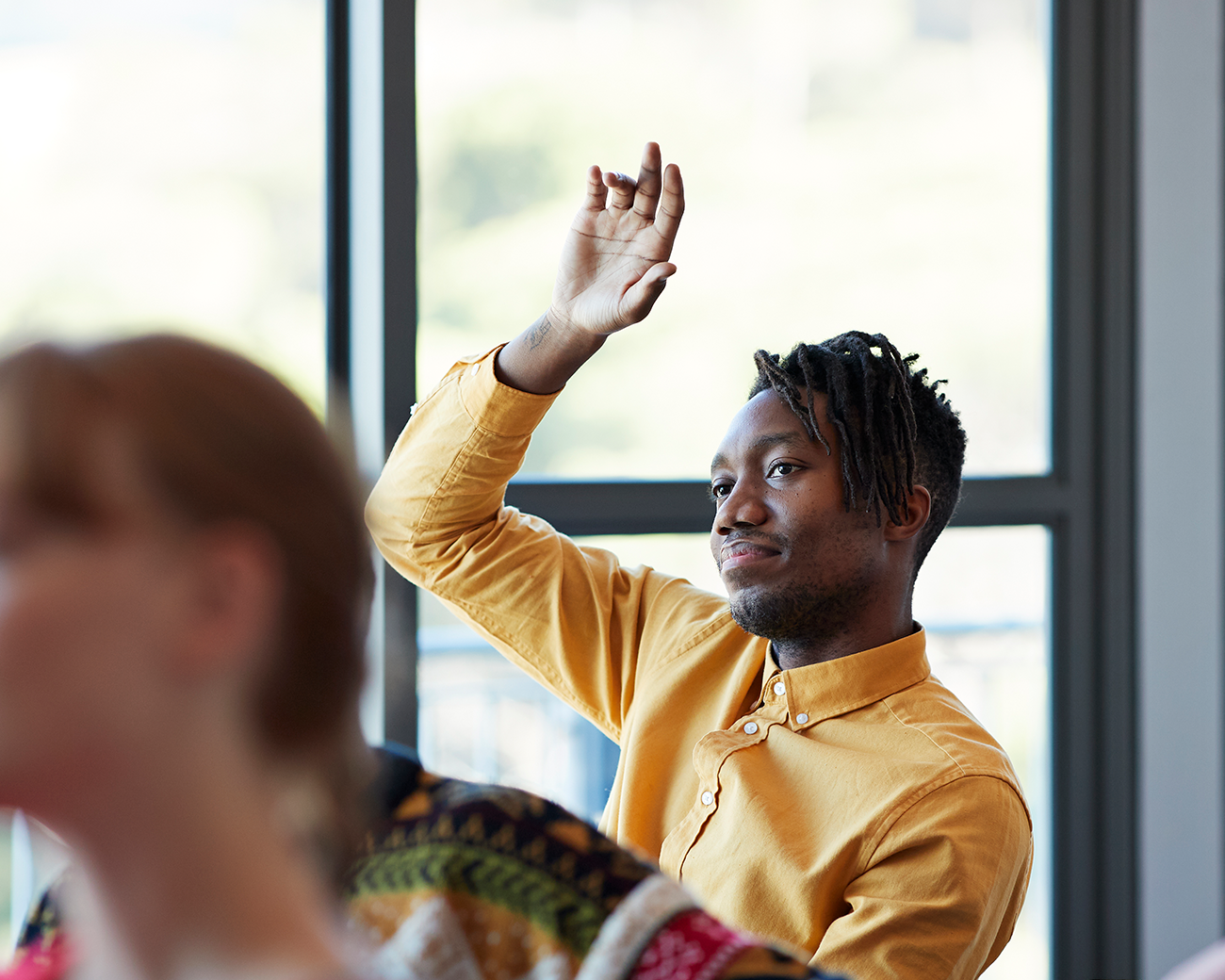 Man in oranje shirt in klassensetting steekt zijn hand op
