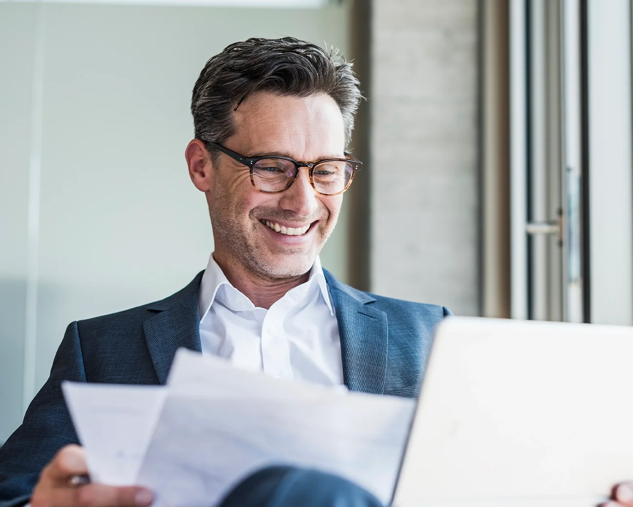 man met laptop op schoot en papieren in zijn handen