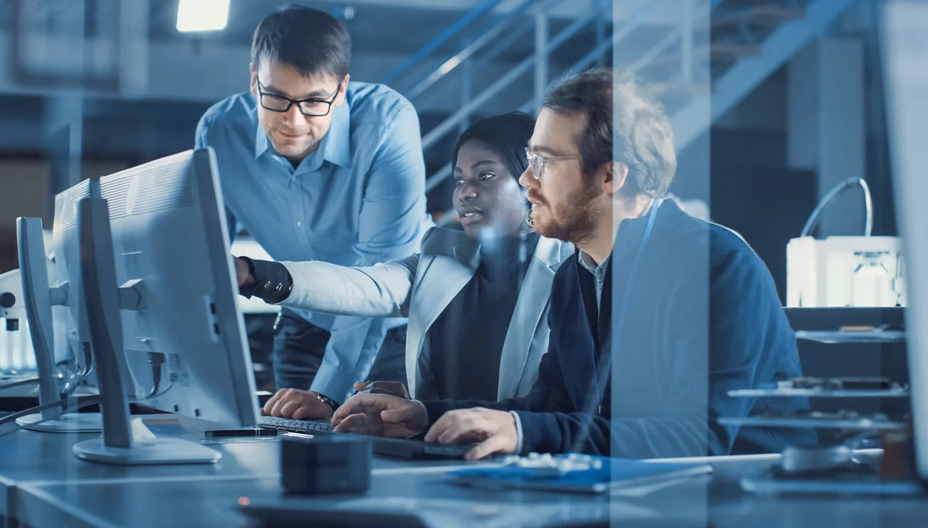 Drie mensen werken samen aan een computer op kantoor.