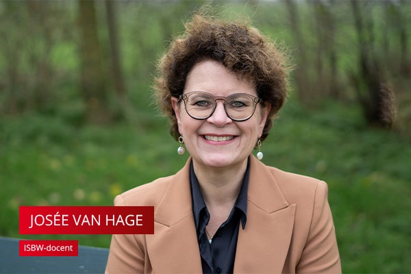 Vrouw met korte bruine krullen en bril met bruin jasje buiten in groene omgeving