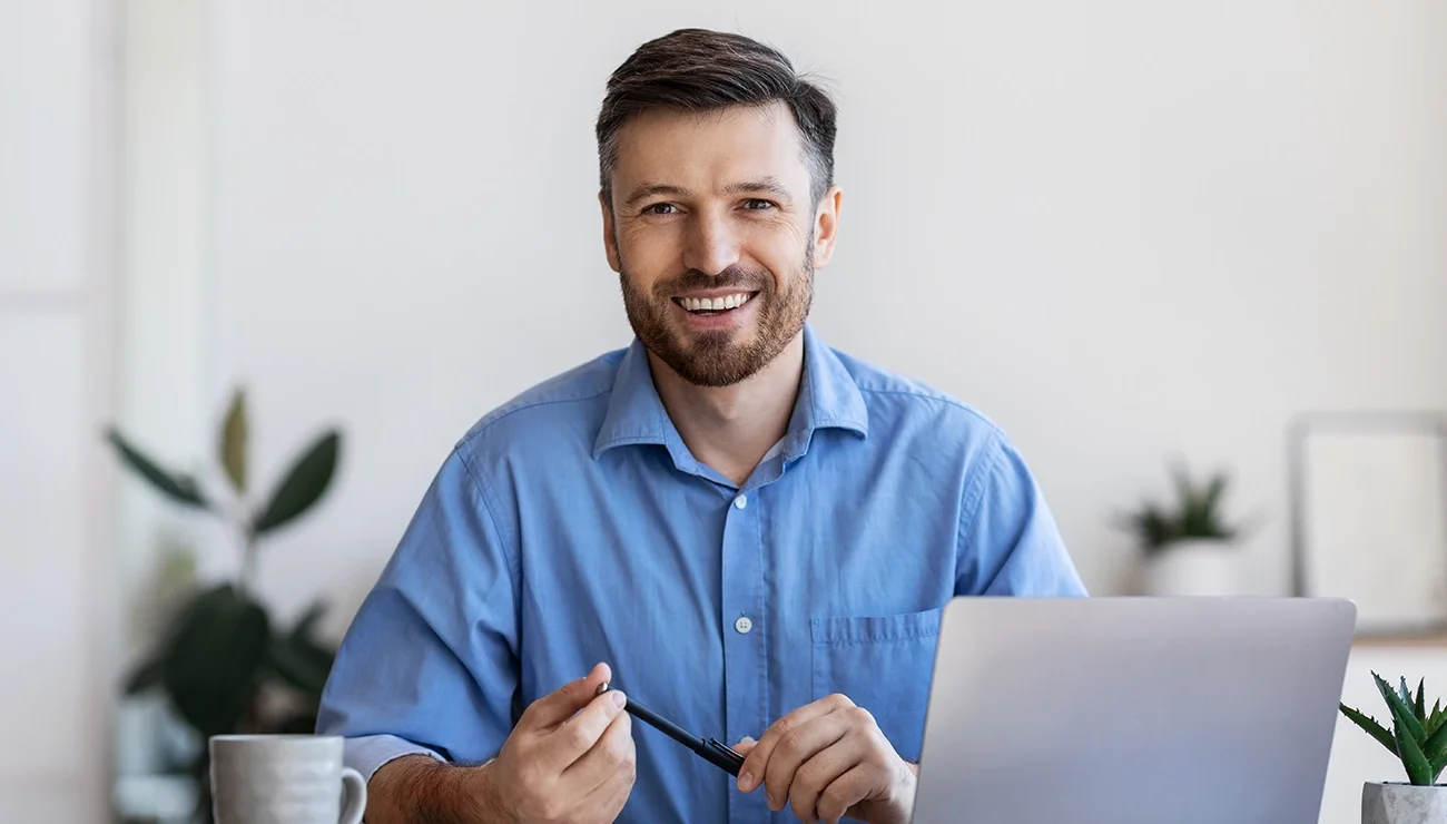 Man achter laptop kijkt lachend in camera