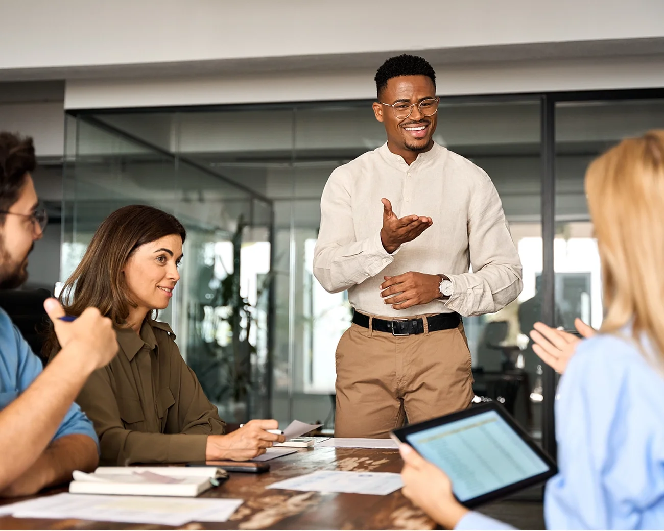 Staande man geeft uitleg aan een groep zittende collega's tijdens een meeting