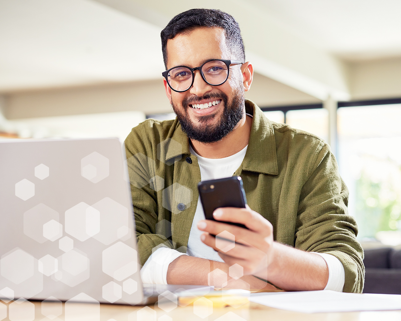 Man met bril achter laptop houdt telefoon in zijn hand