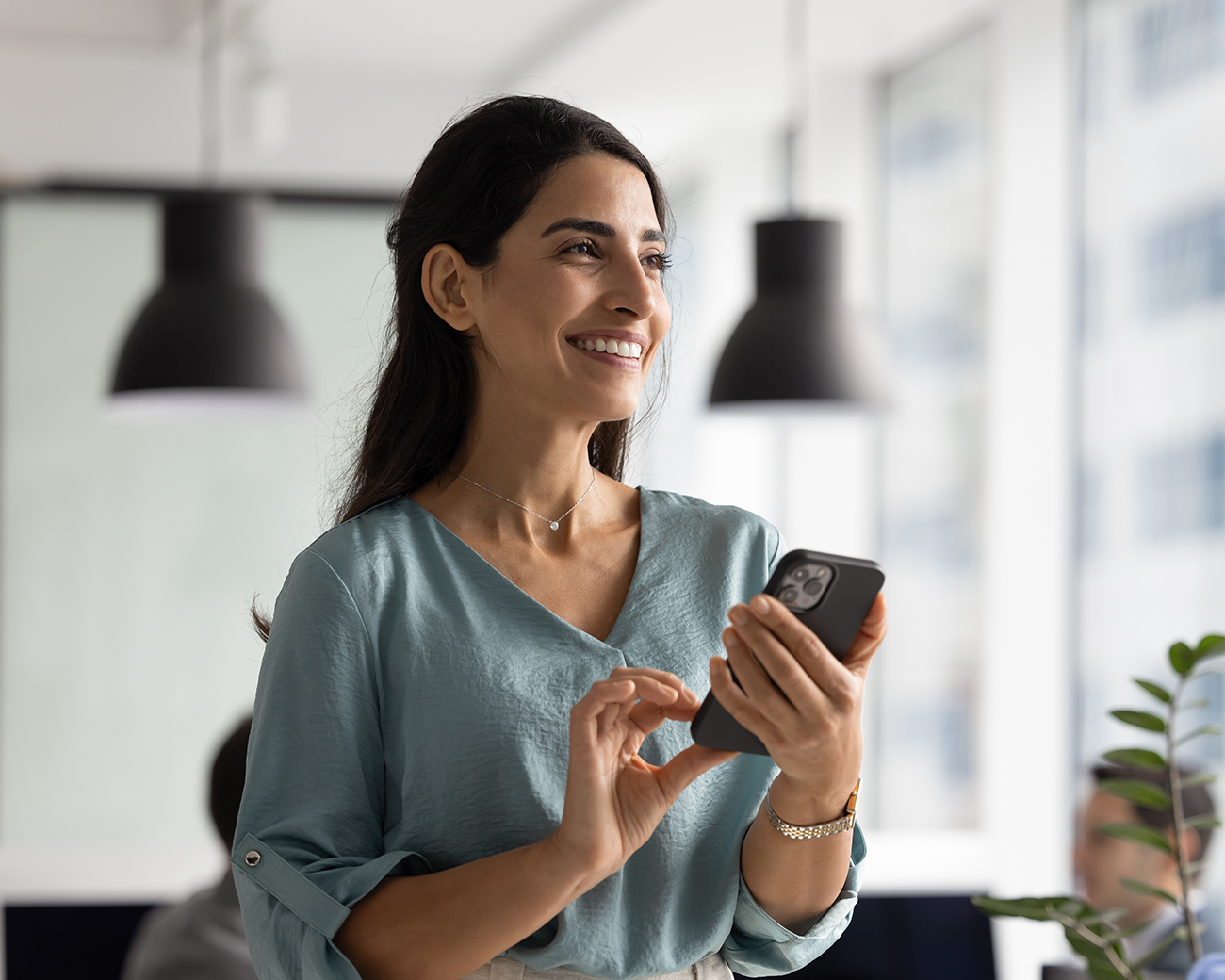 Vrouw kijkt lachend naar rechts met mobiel in haar hand