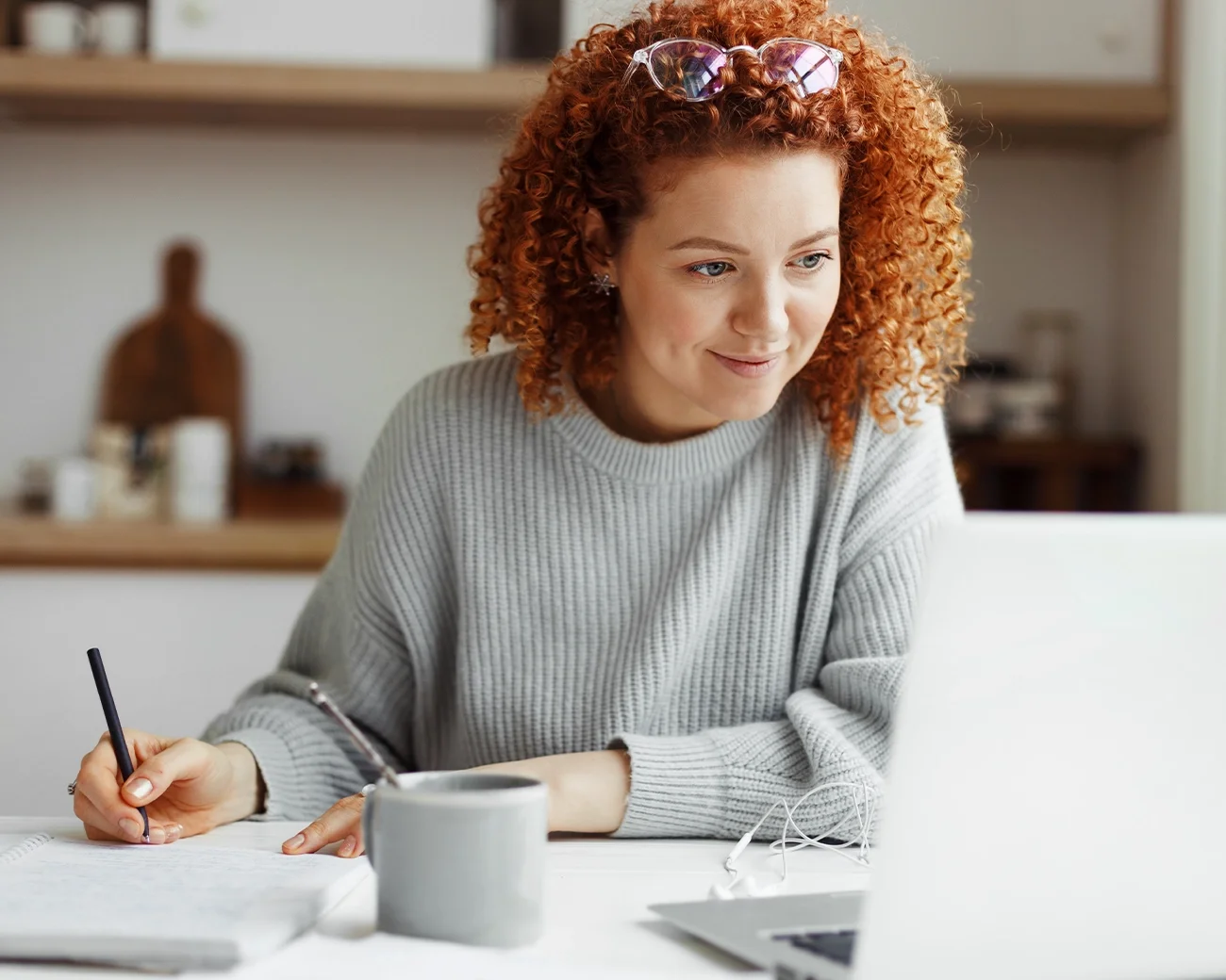 Vrouw volgt een online leeractiviteit en maakt aantekeningen aan tafel