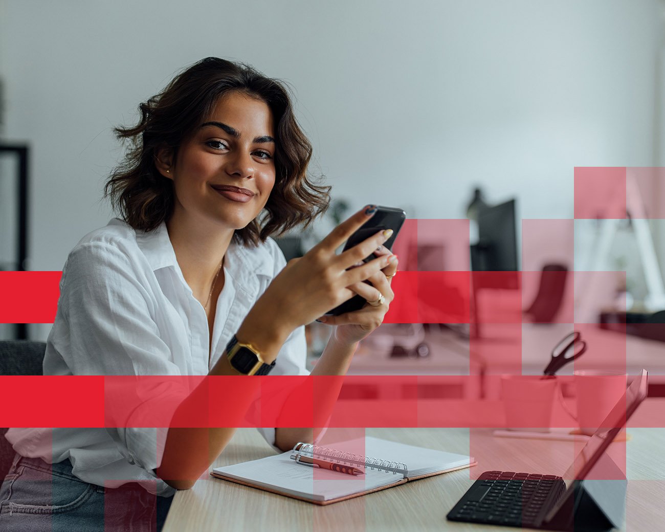 Vrouwelijke medewerker aan bureau met mobiel in de hand