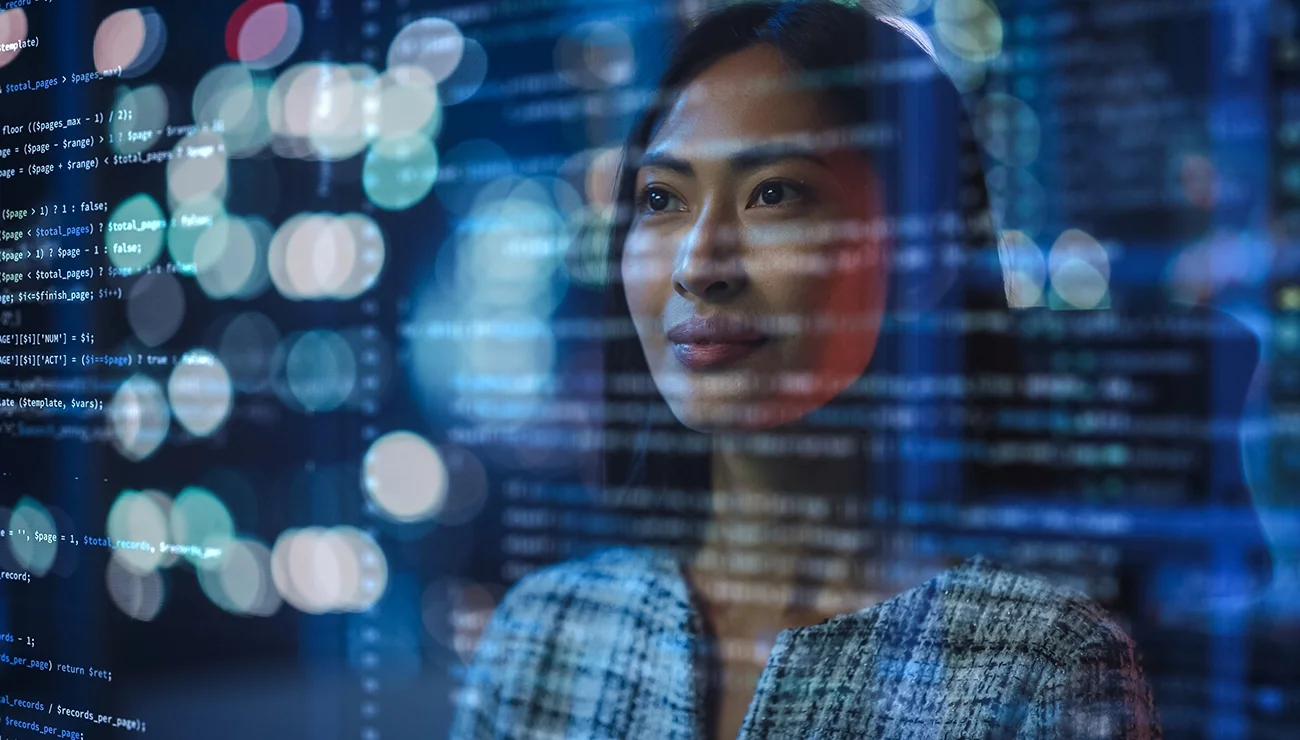 Vrouwelijke tech-ondernemer achter computer, met code als visuele reflectie over haar gezicht