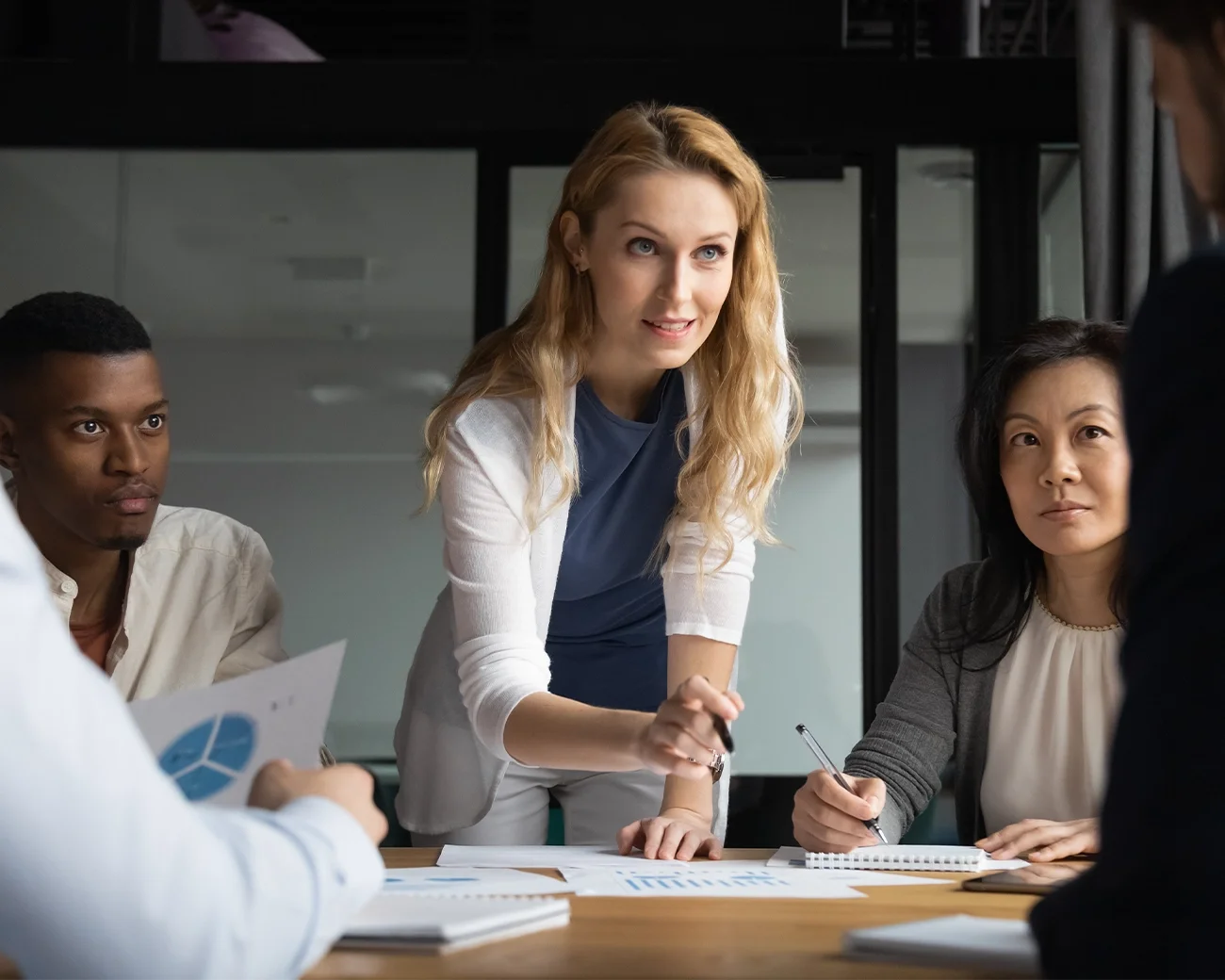 Vrouw staat aan tafel met team eromheen