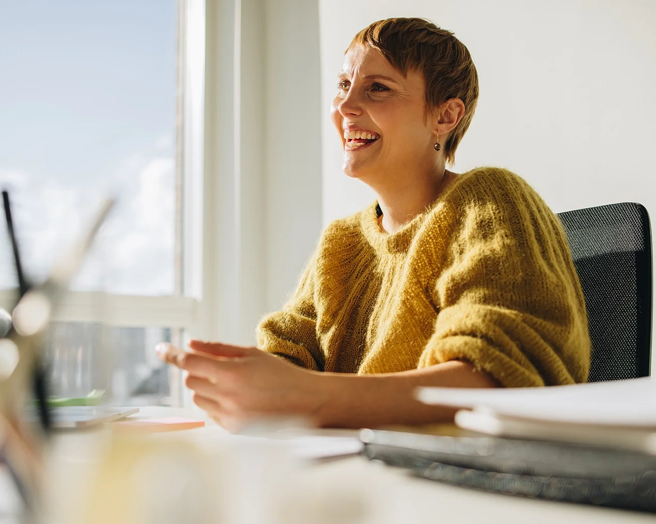 Vrouw in gele trui zit lachend aan haar bureau