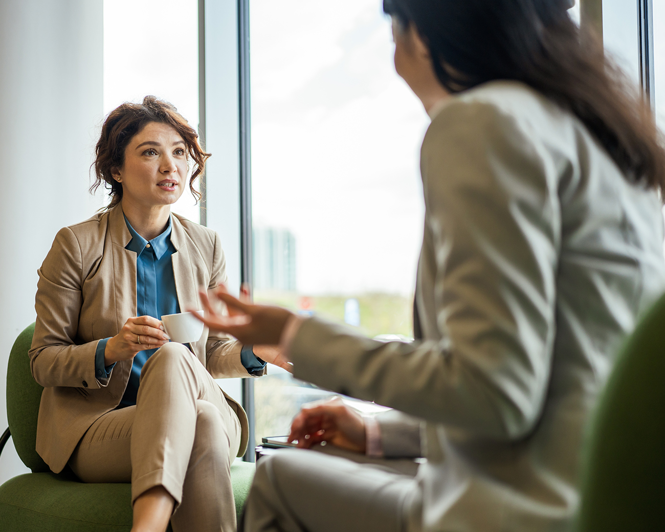 Twee vrouwen in beige kleding in gesprek bij het raam
