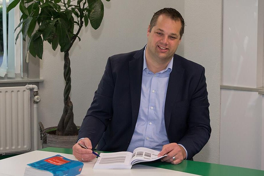 Ed van der Scheer achter een bureau met boek open op tafel