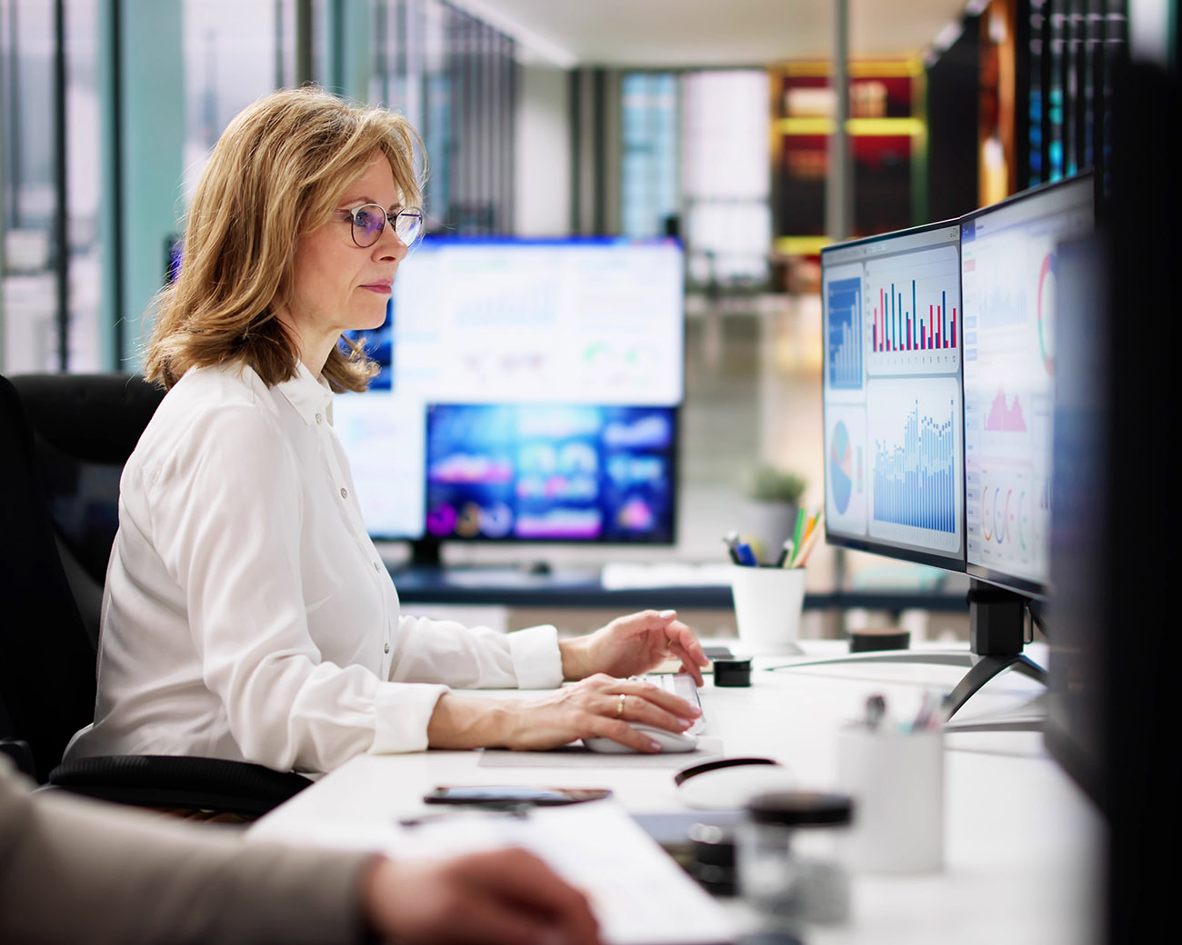 Vrouw achter 2 computerschermen met grafieken en data