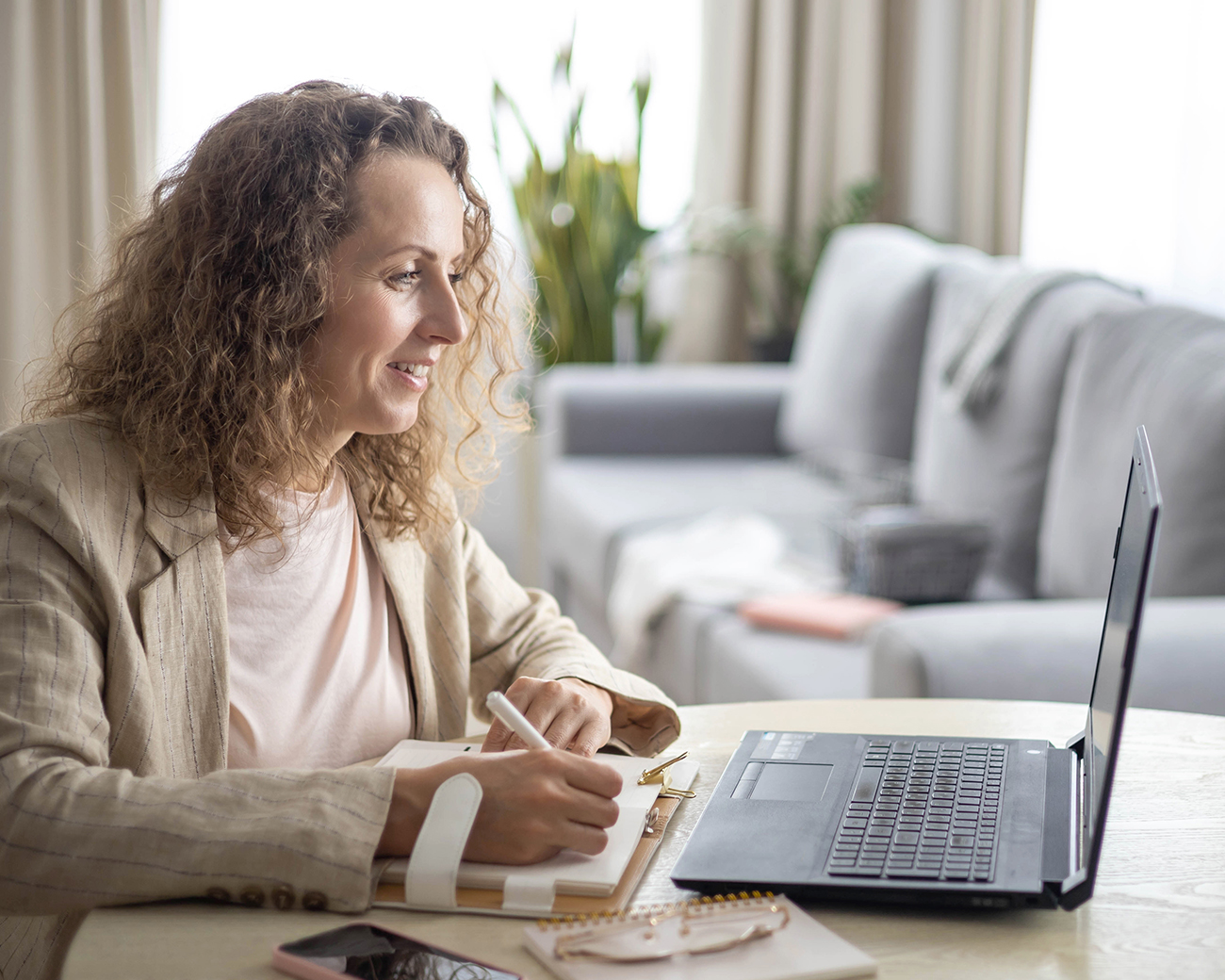 Vrouw met krullen maakt aantekeningen achter haar laptop