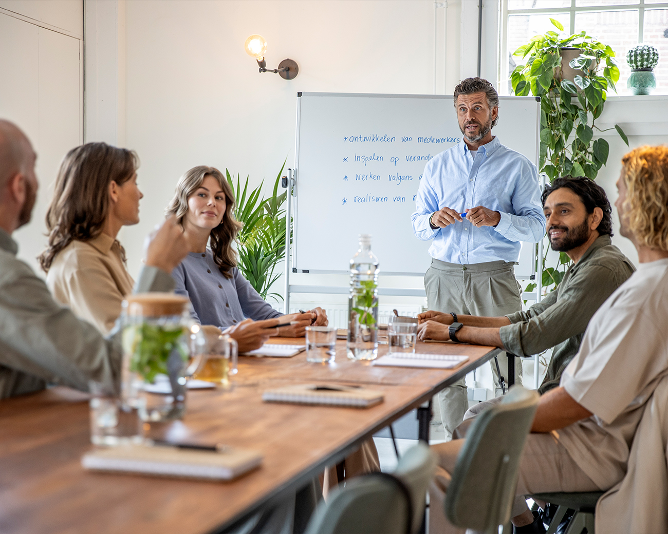 Groep volwassenen aan lange tafel luisterend naar een trainer