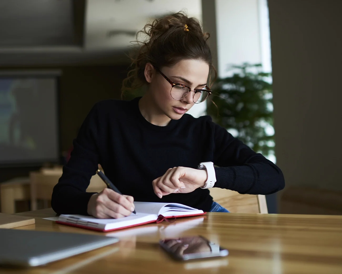 Vrouw schrijft in boek en kijkt op horloge