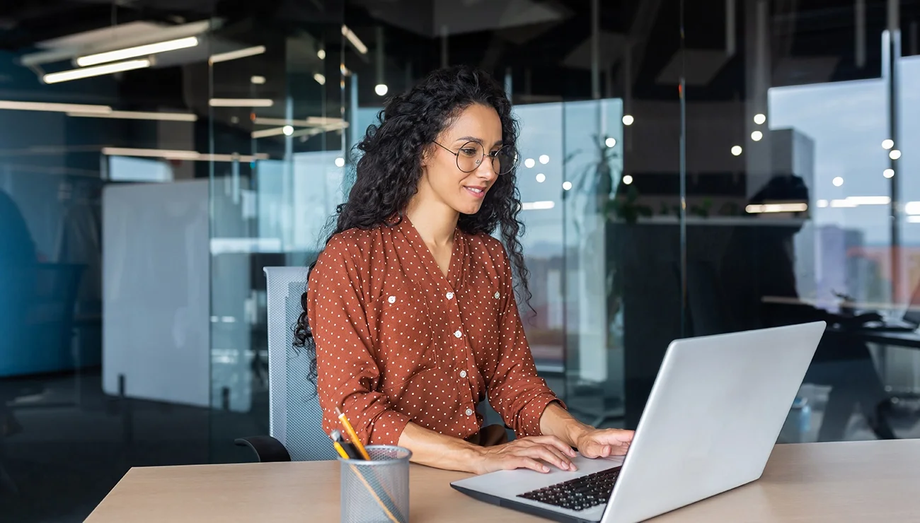 Vrouw zit aan een bureau en werkt op een laptop