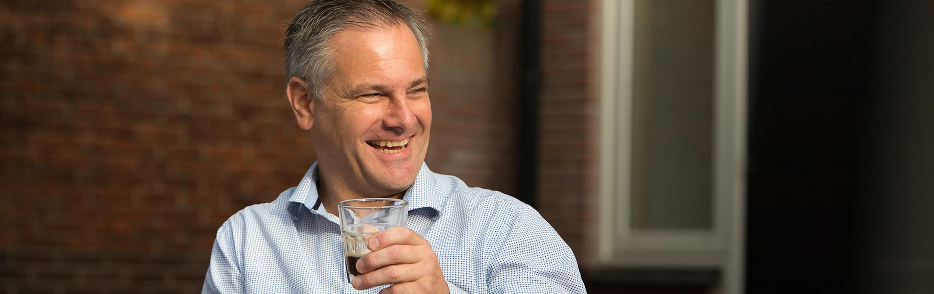 Lachende man met blauw-wit gestreept hemd en glas koffie in zijn hand