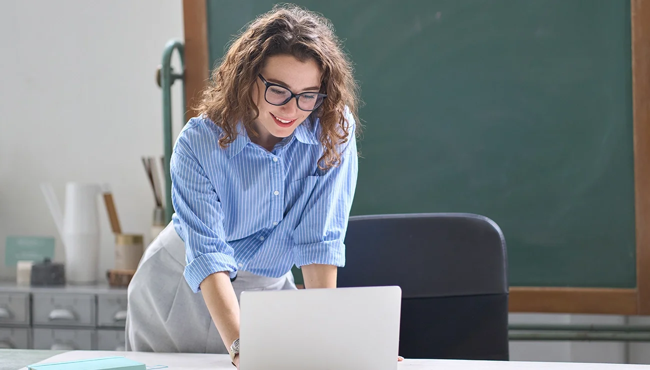 Jonge vrouw met krullen en bril kijkt naar laptop voor schoolbord