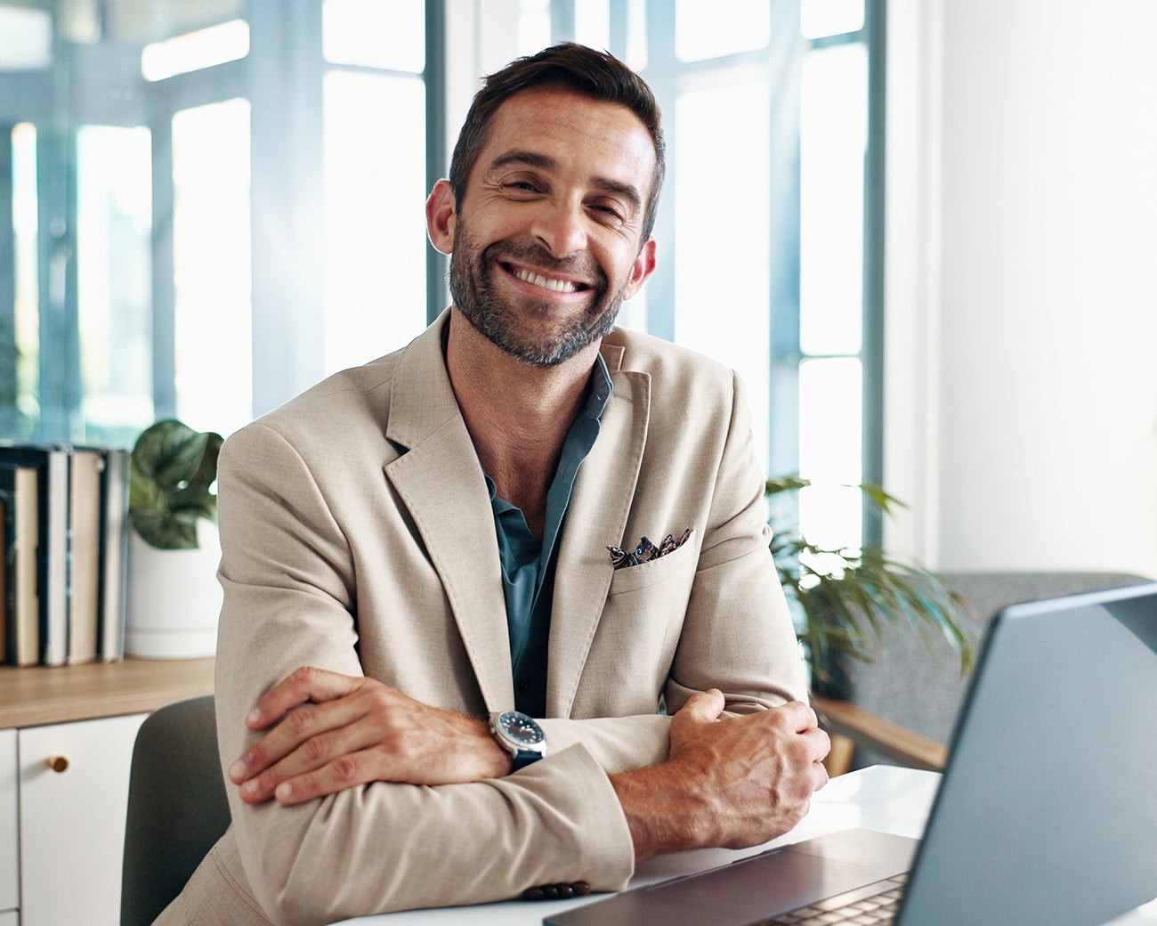 Man in beige pak lacht van achter laptop